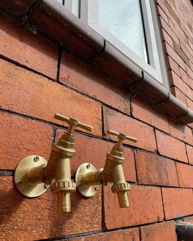 Bronze outdoor plumbing faucets on brick wall for garden or exterior use. Expert plumbing services provided.
